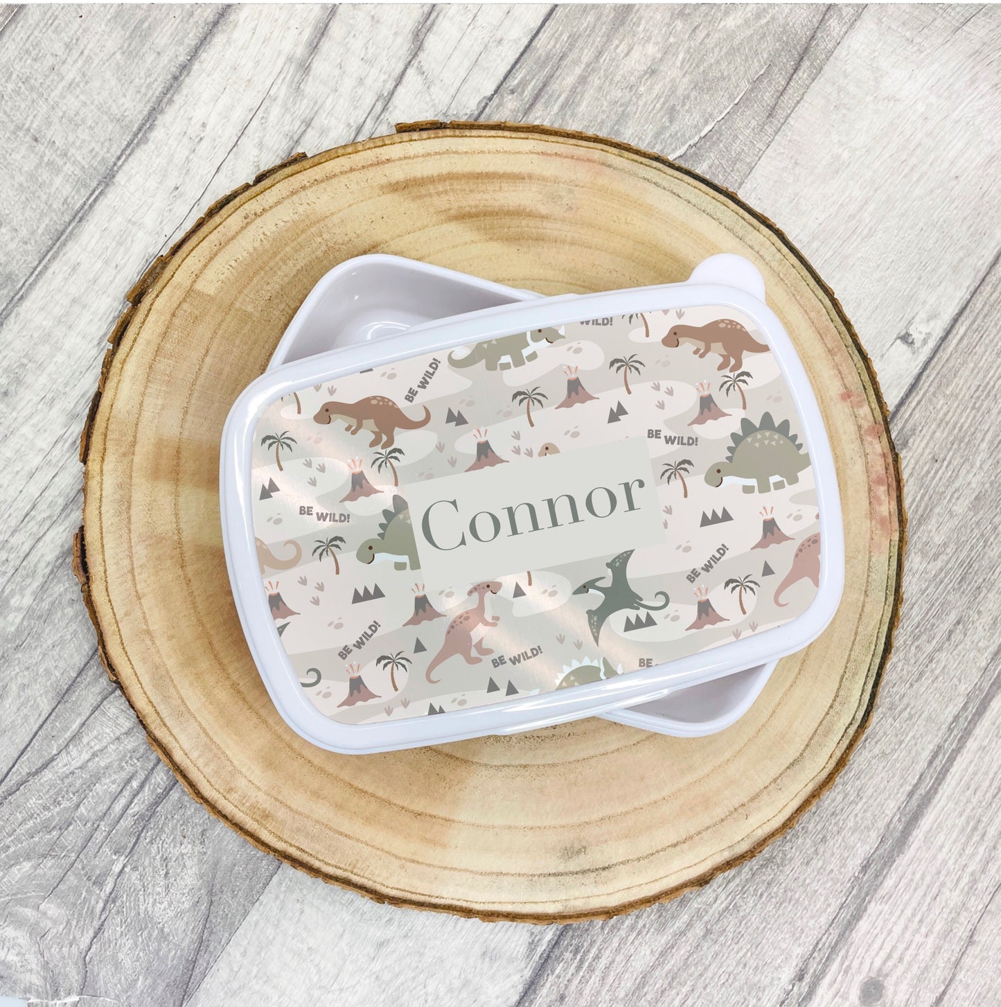 This is a white lunch box with a snap on lid. The lid is printed with a pattern of dinosaurs with a name in the middle.