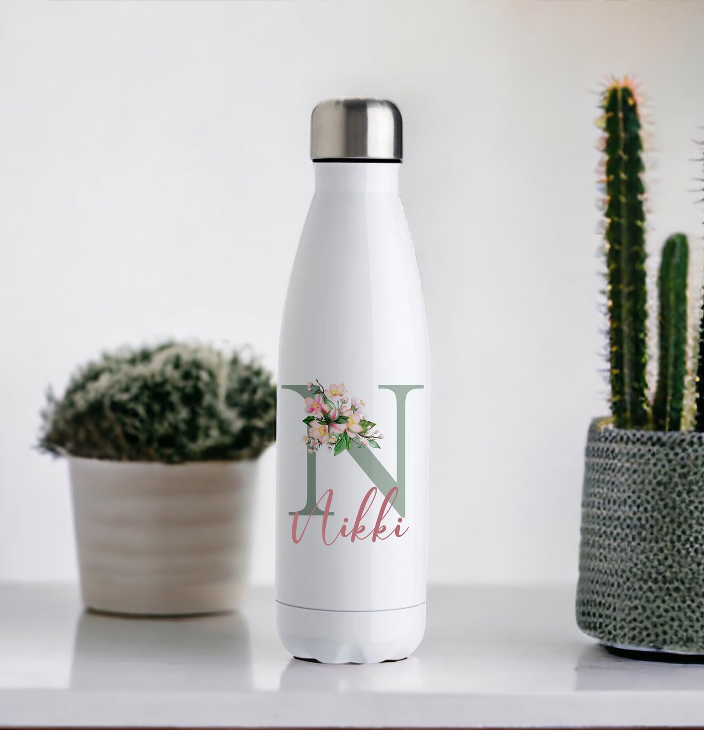 This is a white chill flask. It is designed to keep drinks cooler for longer. These flasks hold 500ml of liquid. Printed on the flask is a sage green initial decorated with pink flowers and personalised with a name