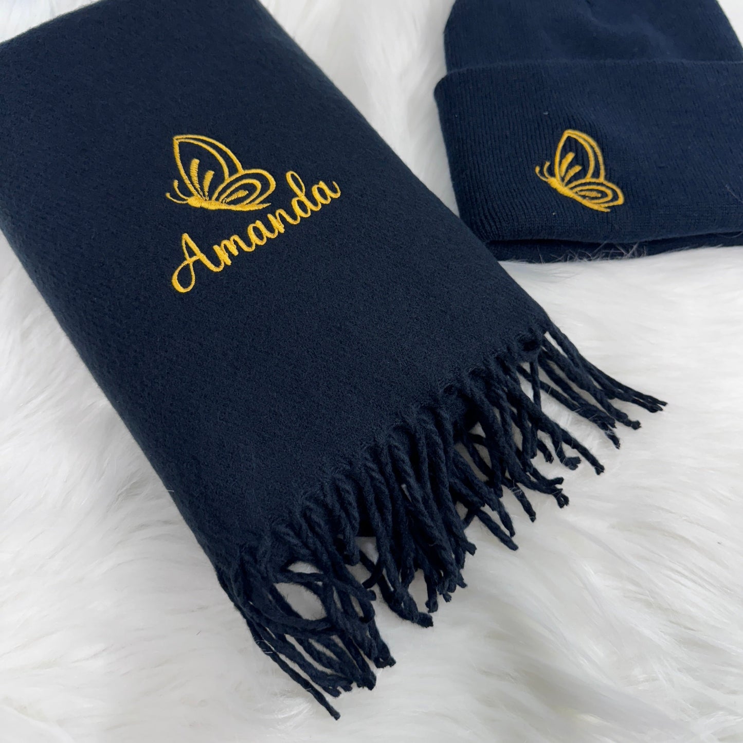This is a navy hat and scarf set. Embroidered on the hat to the side is a golden butterfly design. On the scarf is also the matching butterfly design with the name embroidered below also in gold
