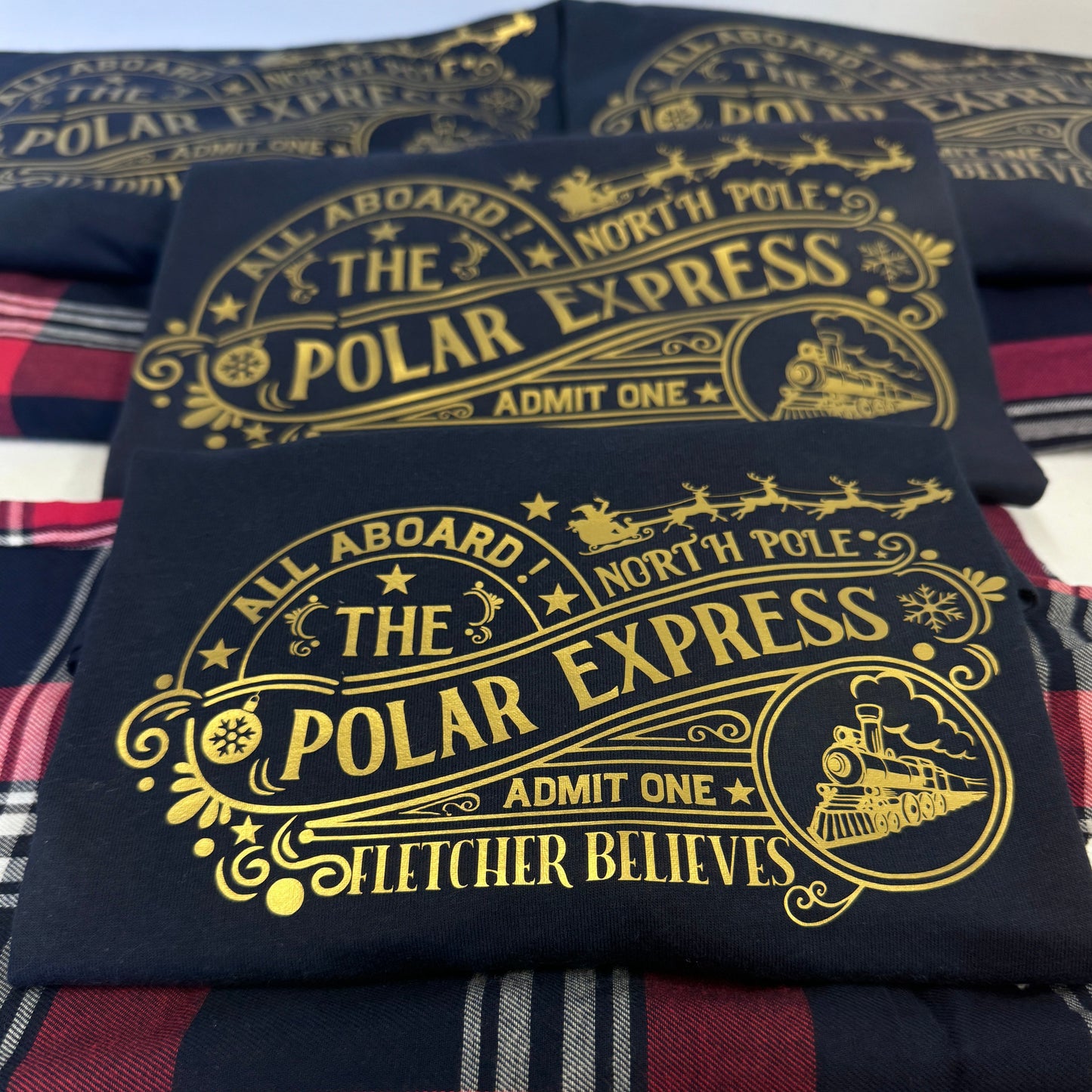 All aboard the Polar Express! Matching family outfits featuring a navy tshirt and tartan red trouser. The tshirt is vinyl printed in gold with an eye catching polar express - north pole design. personalised with a name too