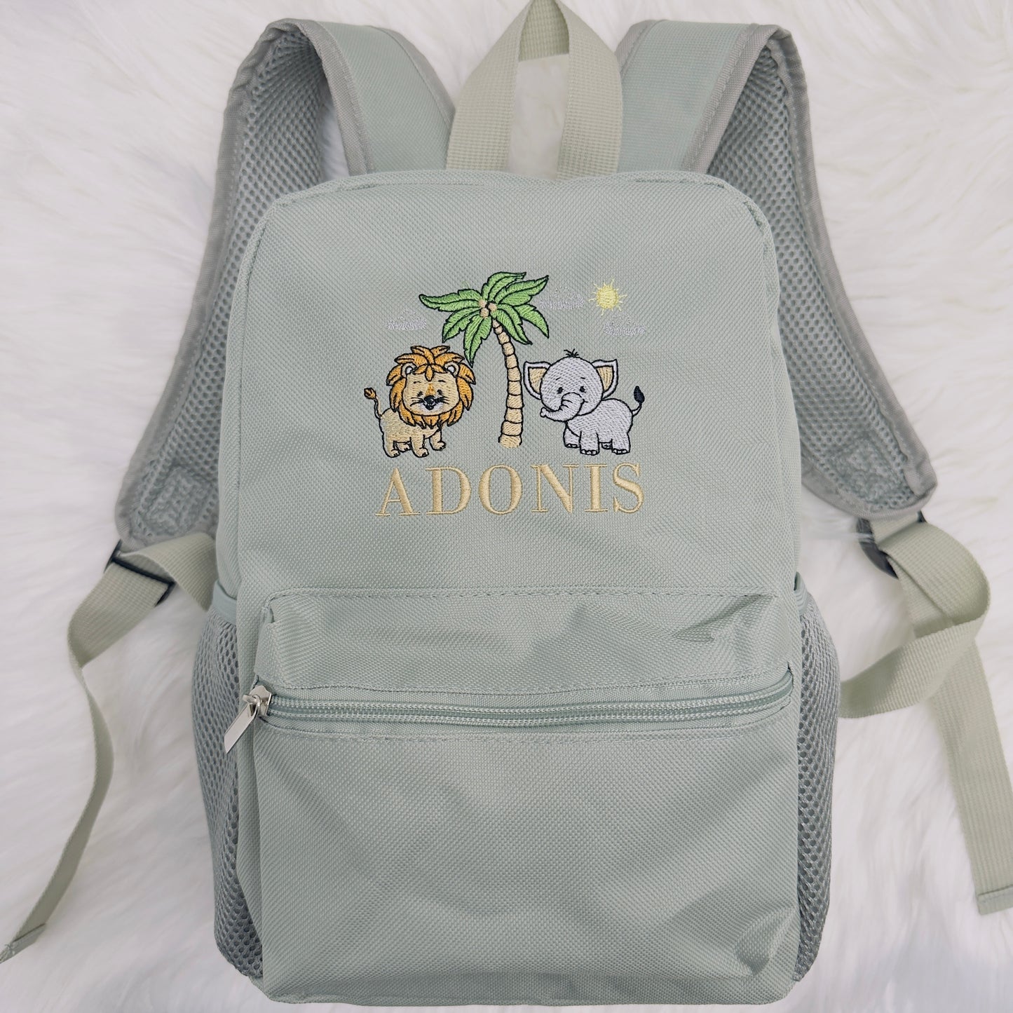 Introducing our new backpack design featuring a Lion and Elephant with a palm tree.
These bags measure 29.5 x 21cm. They have a handy elasticated drinks bottle holder on each side. The main compartment has a twin zip, there is also a small front compartment too.
This back is super comfy to carry with adjustable, padded straps and also has a small peg loop to hang from.
Each bag can be personalised with your child's name or you can choose to leave it blank.
Available in Sage, Nude, Blue and Pink. Sim