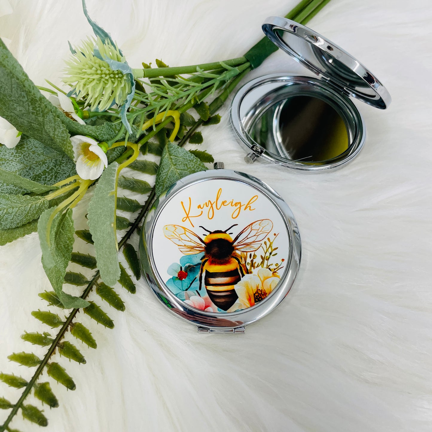 This is a silver compact mirror with a push button opening. On the top of the mirror a beautiful, vibrant bee is printed with blue and yellow flowers. A name is also curved around the top. Lovely personalised gift for her.