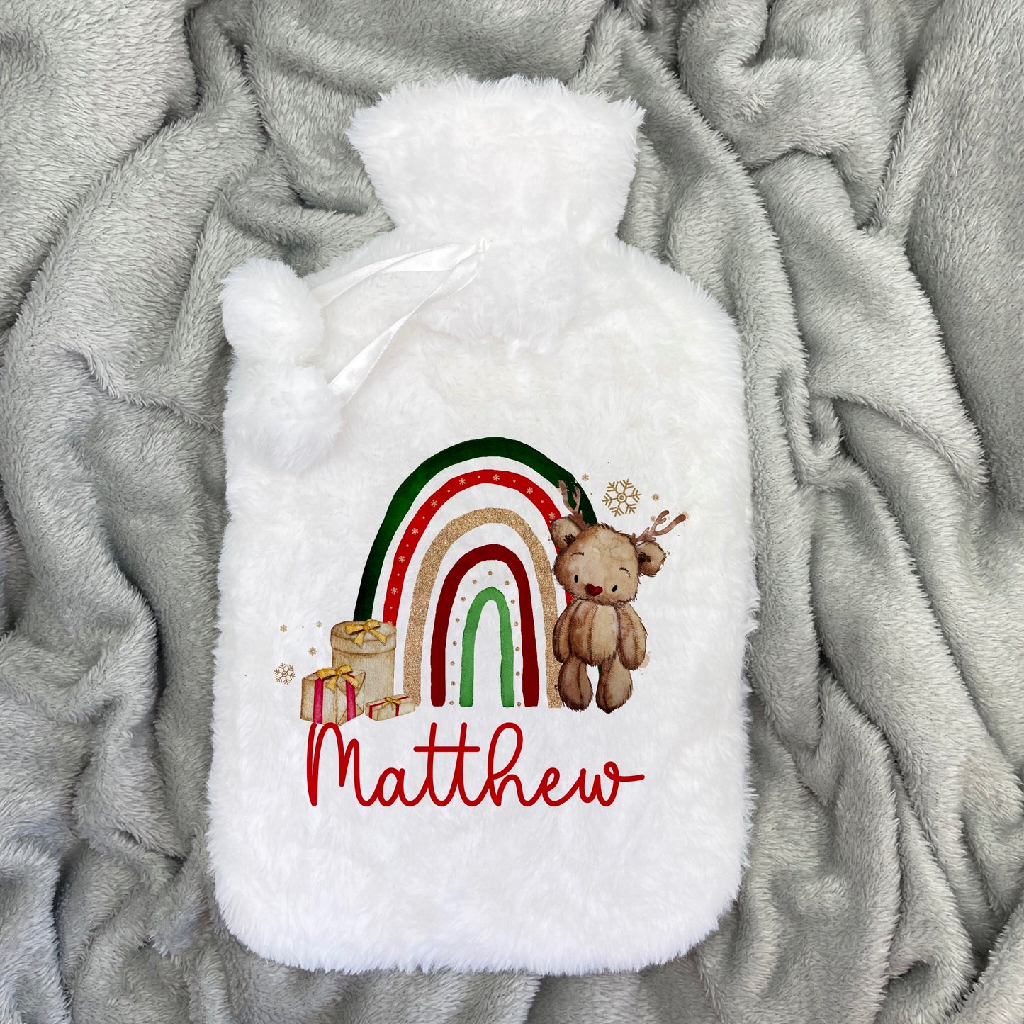 Our little christmas bear is the custest! This is a white hot water bottle with a festive rainbow printed on the front. Along with the rainbow is a little stack of gifts and a little bear to the side. Personalised with a name this is a lovely gift.