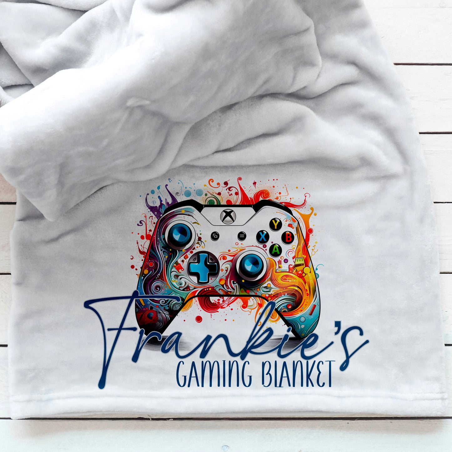 This is a grey, thick, luxury blanket. The blanket has been personalised with an xbox controller painted with swirling, bright colours. A name is printed across the controller with gaming blanket below. Great gamer gift idea for boy or girl
