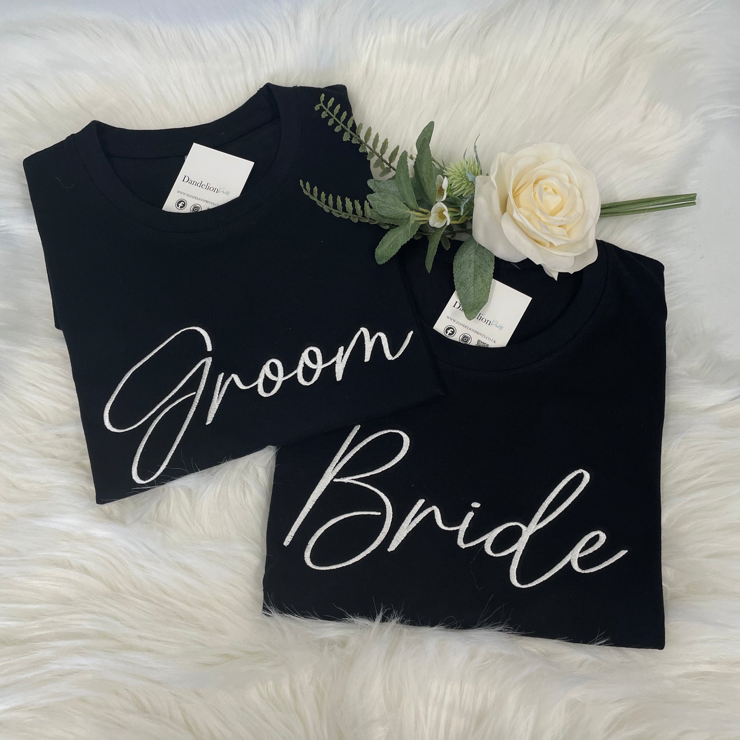 This is a photo of two tshirts in black. Both tshirts are embroidered on the front, one with Bride and the other with Groom. This is a matching set for a newly married couple ready for their next chapter.