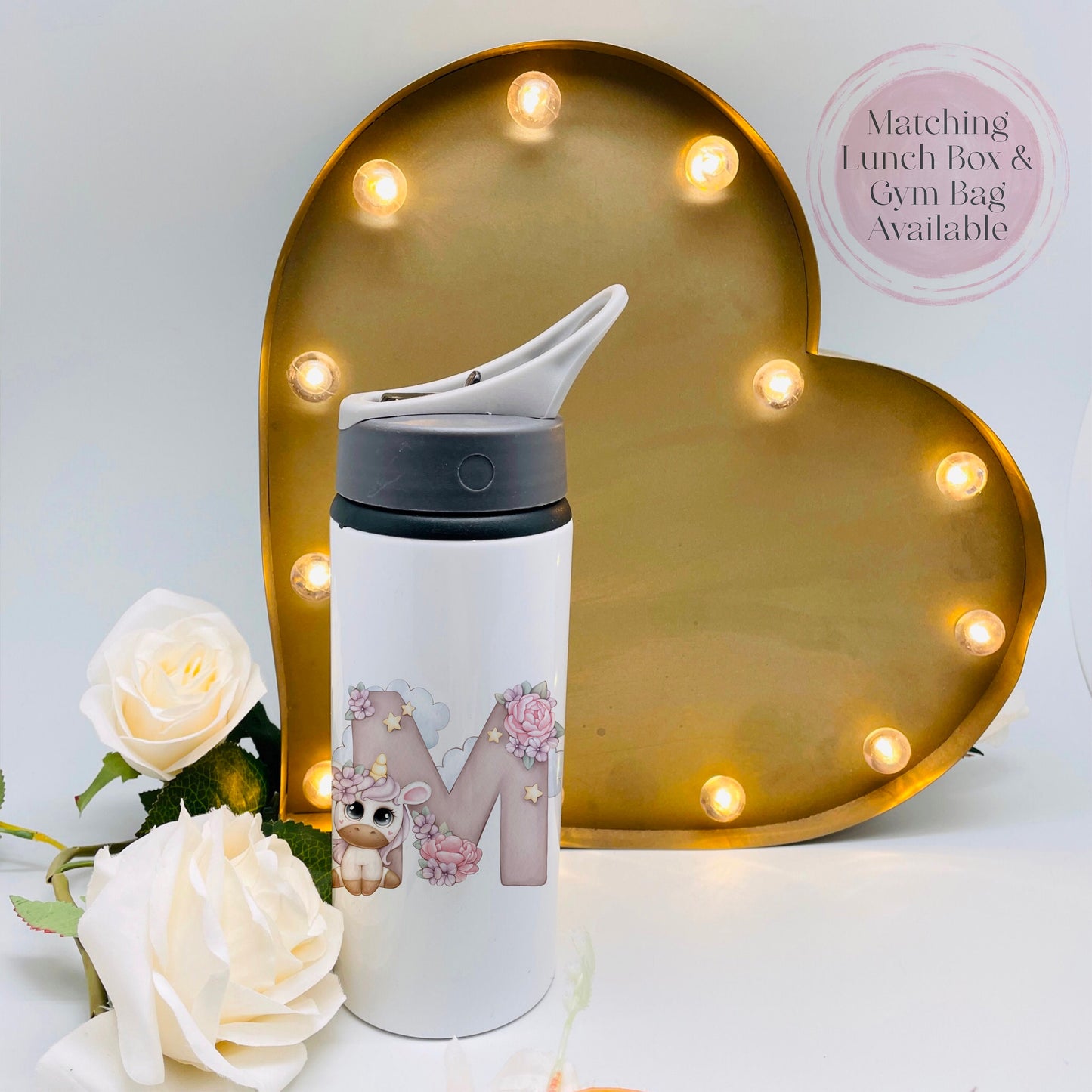 Image of a white metal flask with black top and drinking spout. The main body has printed initial with flowers and clouds on along with a unicorn with big eyes and flowers in its hair.