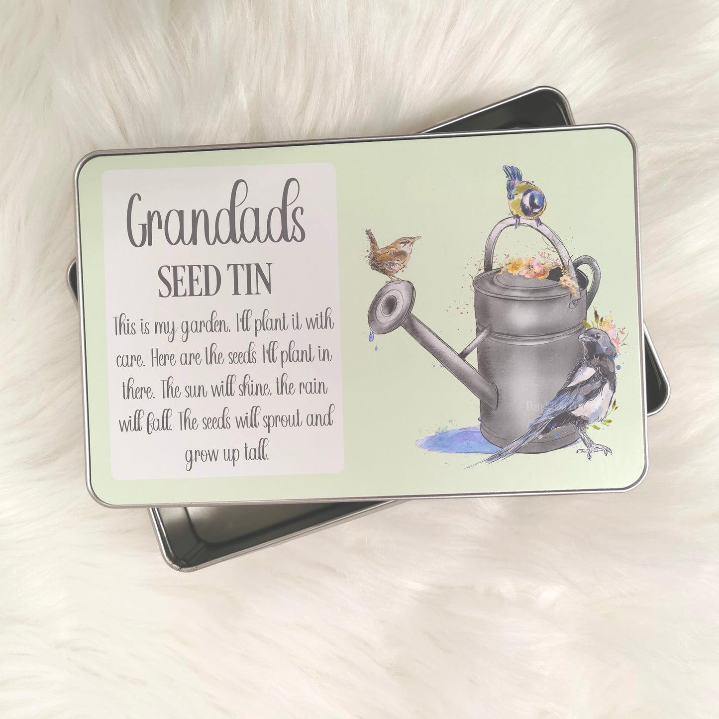 This is an aluminium tin with a full printed lid. The print has a pale green background with a picture of a metal watering can and birds around it. The tin is designed for those that love their gardens including grandads and nans.