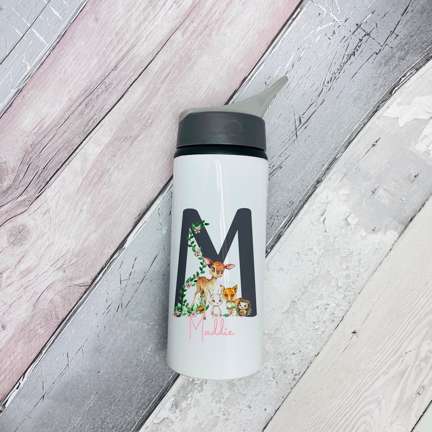 Image of a white metal flask with black top and drinking spout. The main body has a printed woodland scene with a deer and a rabbit along with the name Maddie