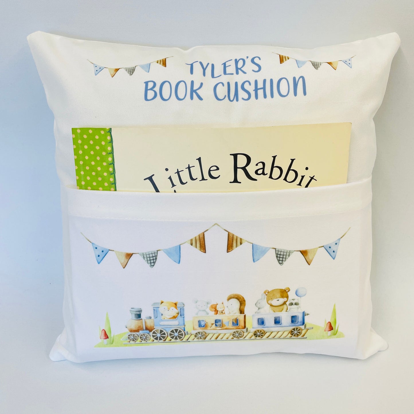 A super soft white cushion with a pocket on the front. The pocket keeps a book nice and safe until the next story time. This is printed with a cute watercolour train with little animals riding the train. The top part of the cushion has a name