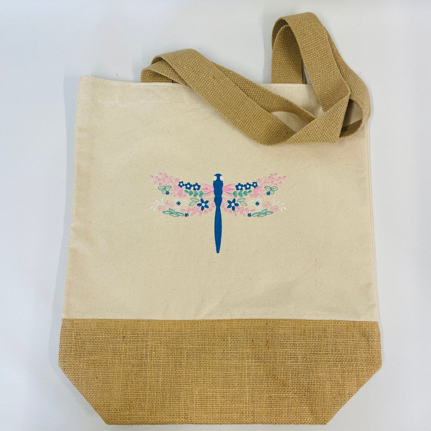 Dragonfly embroidered tote bag. This is a cotton canvas material with jute handles and jute base. The dragonfly is embroidered in blue, pink and sage.