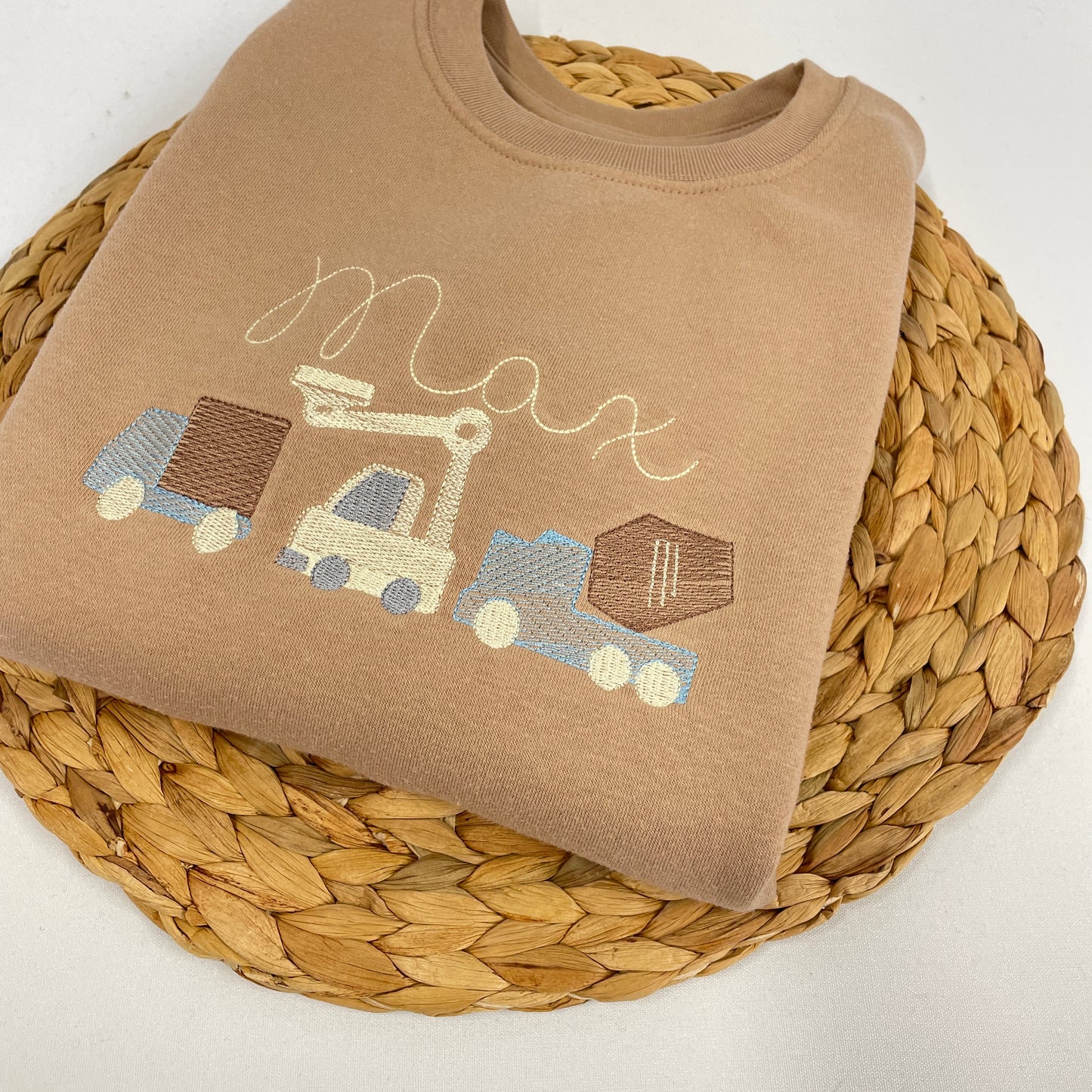 This is a brown sweater with fleece lining. Embroidered on the front of the sweater is three construction trucks, a van, a digger and a cement mixer. There is a name above the image also embroidered.