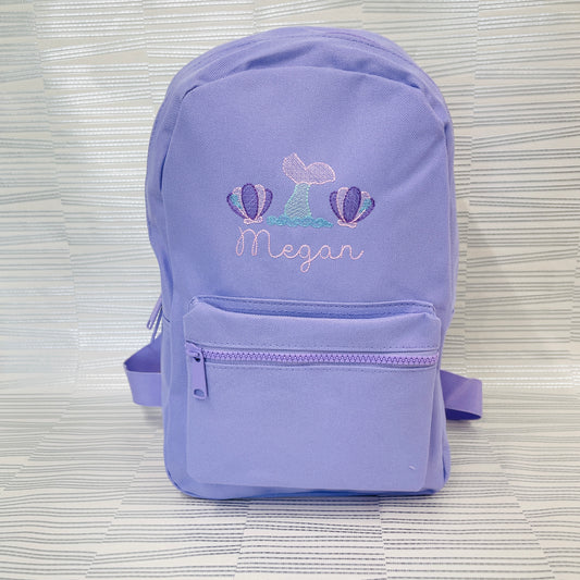 This is a lilac backpack with embroidery on the front. The embroidery is Mermaid theme with two shells either side of a mermaid tail. The colours of the design are pink and purple with a mint mermaid tail and blue water splashes. There is a name also. A lovely girls backpack for school or nursery.