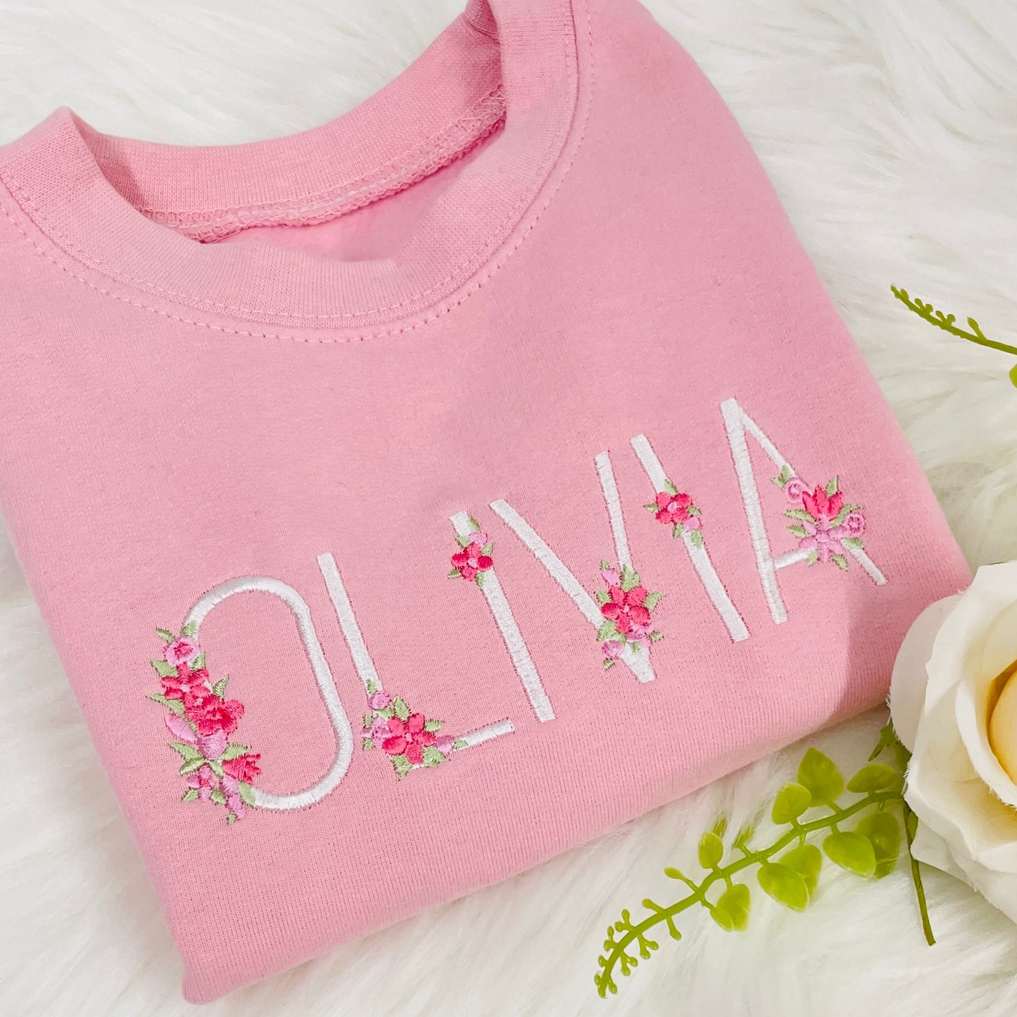 This is a beautiful girls sweater with a name embroidered in white on the chest. The name is decorated with dainty pink florals with sage leaves. The sweater is pink in colour. The sweater is fleece lined and super comfortable. personalised girl gift