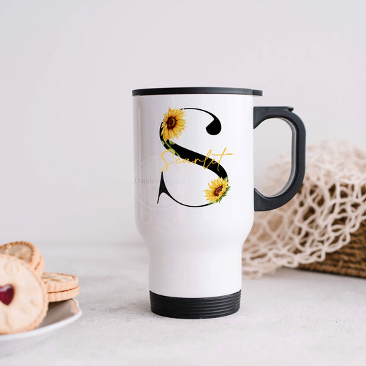 This is an image of a travel mug standing on a kitchen worktop. The travel mug is stainless steel with a handle and lid. printed on both sides is a black initial with sunflowers growing around it. This is personalised making it a great gift