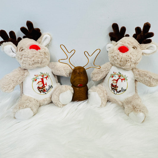 Giant reindeer teddy with its belly printed with the design. The print consists of a Christmas garland with a Father Christmas in the middle. To his right is an alphabetical letter and to the bottom right at an angle is the full name.