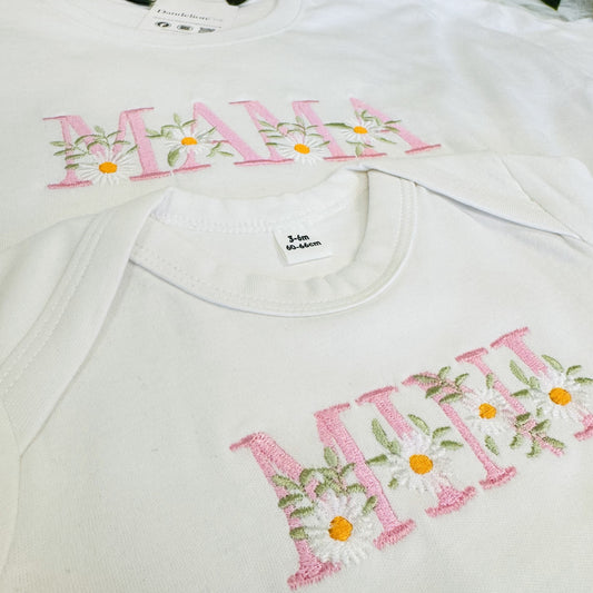 This is a photo of two matching t-shirts. One t-shirt is for an adult and has embroidered on the chest MAMA with flowers. The other t-shirt is for a baby which has MINI embroidered with flowers too. Matching set for mum and baby