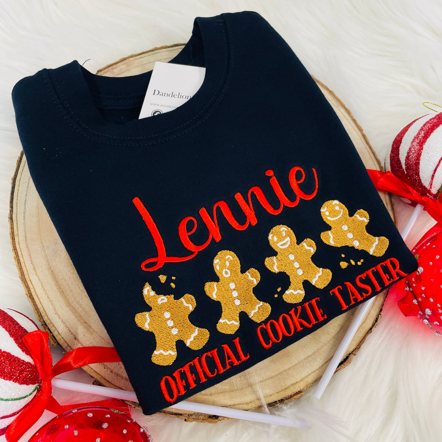 The embroidered design on the front of this sweater consists of four gingerbread men, two have been bitten but they all have a funny little face. The design has a name embroidered above it and 'Official cookie taster' embroidered below.