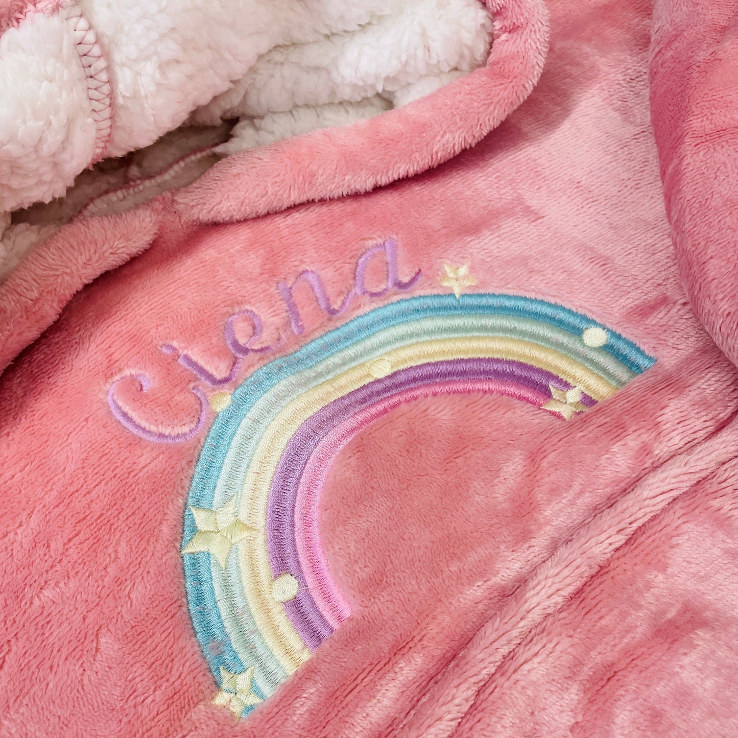 This is a girls oversized hoodie with a rainbow embroidered on the front. Above the rainbow is a name. The hoodies are extremely soft and warm with sherpa lining. They have a pocket on the front and a hood too.