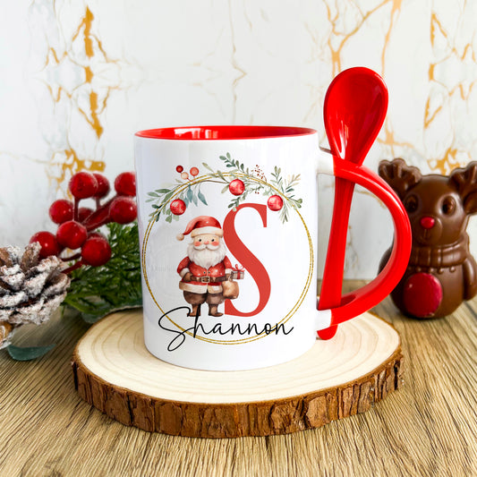 This is a white mug with red inner / handle. Theres a slit in the handle to allow a red spoon to sit in. On the front is the design consisting of a Christmas garland and father Christmas figure on the inside. There is an alphabetical letter and name