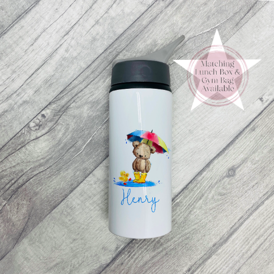 Image of a white metal flask with black top and drinking spout. The main body has  printed image of a teddy bear, wearing wellies holding an umbrella stood in a puddle. There is also the name Henry