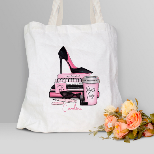 White shopping bag with Boss Lady design printed on. Striking pink and black colours featuring a pink stiletto placed on a stack of books with girlie accessories surrounding the design.