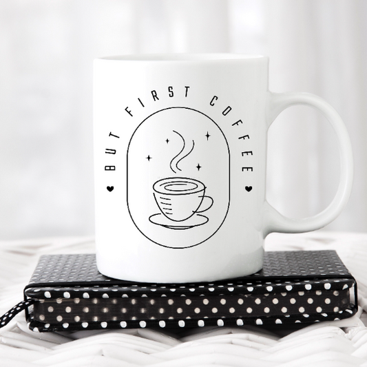 Enjoy your morning coffee with an 11oz white ceramic mug with an oval design printed. Inside the oval is an outlined coffee image with steam and stars. Around the outside the oval image are the words BUT FIRST COFFEE