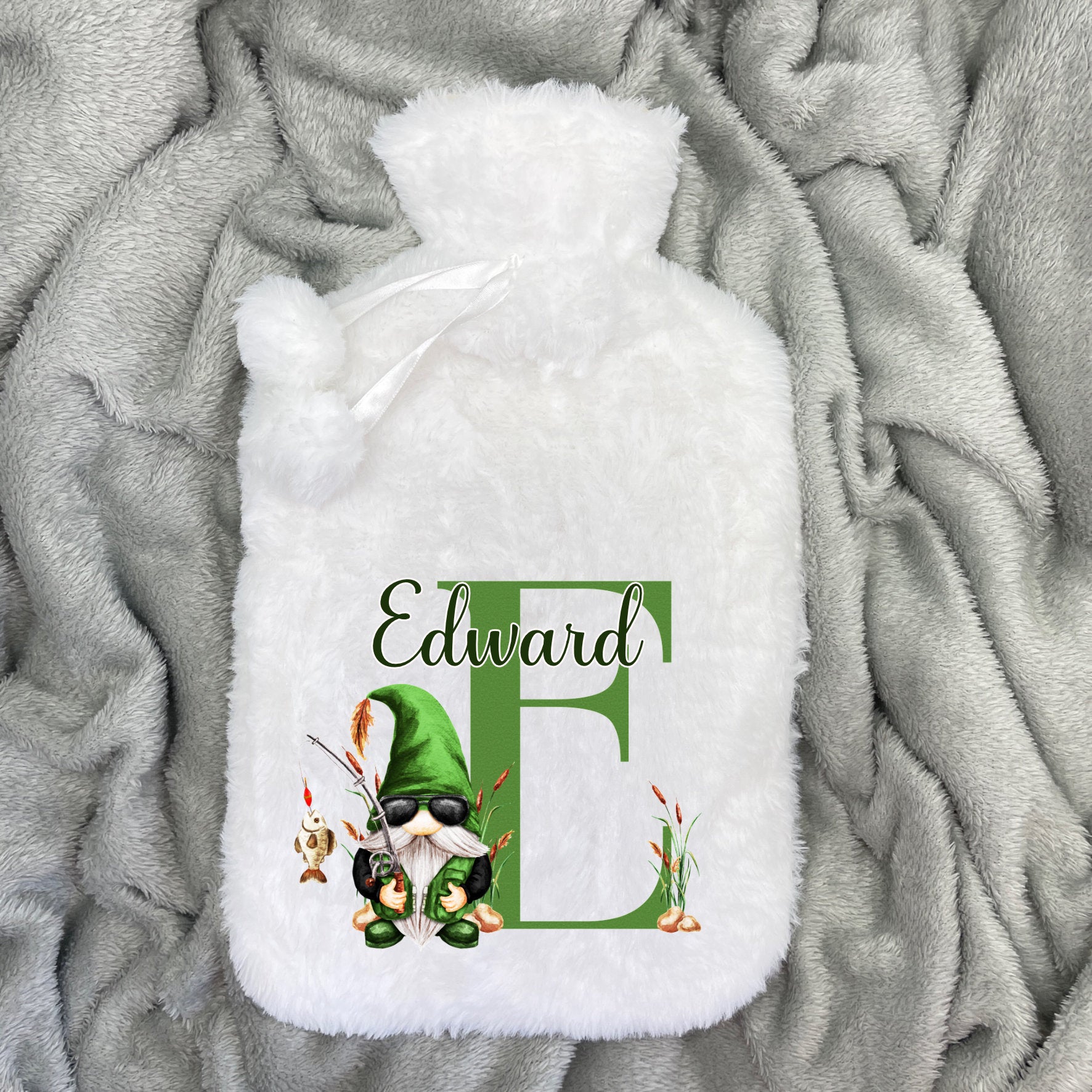 This white hot water bottle is printed with a cool fishing gonk. The gonk is wearing sunglasses, all green clothing with a fishing rod in his hand and pond reeds around him. There is a big initial behind the gonk and a name printed across the front.