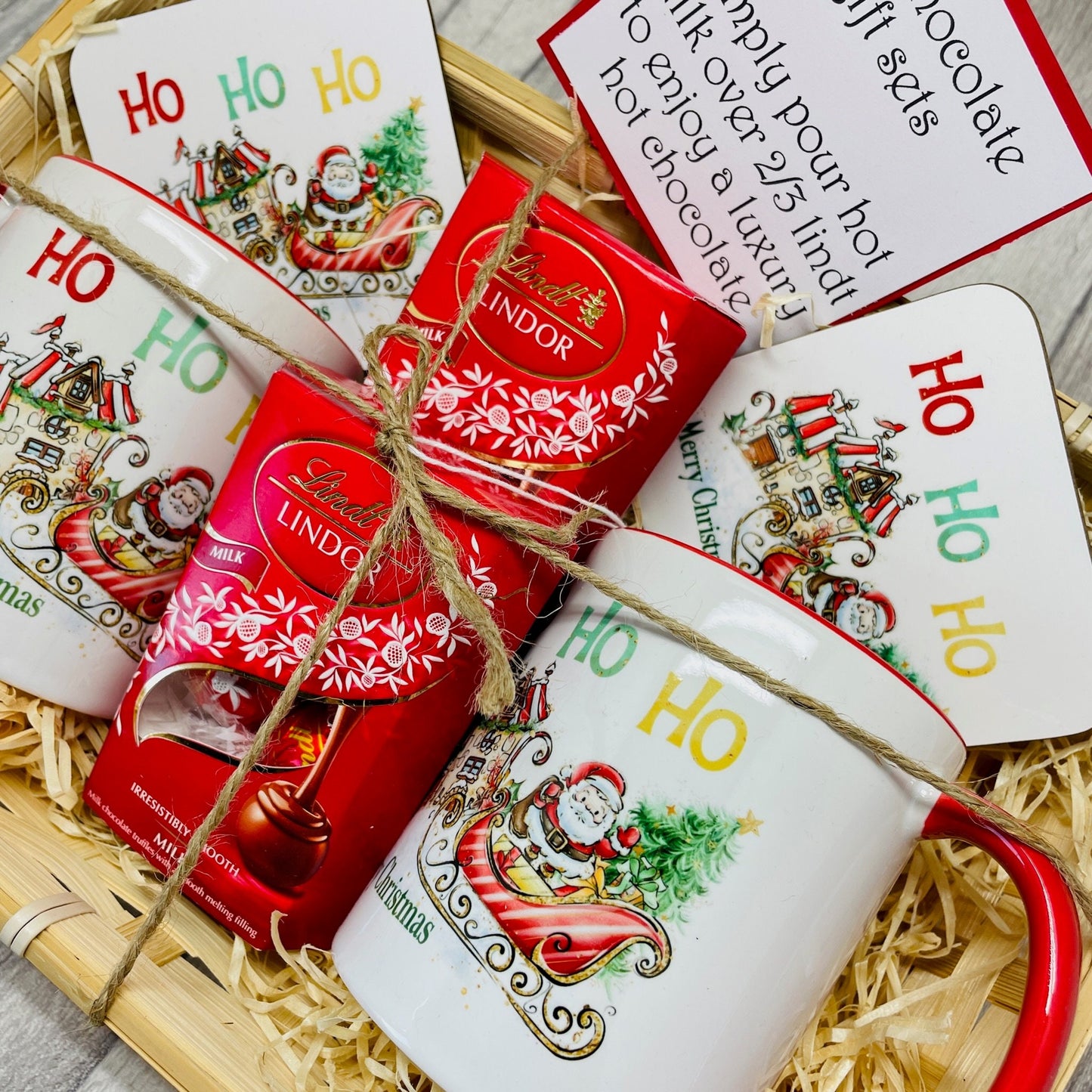 Christmas gift set in a wicker basket filled with a mug, coaster and Lindt chocolates. The design on the mug is Santa on his sleigh heading to a candy cane house to deliver presents. Ideal Christmas Eve gift. Stocking filler.