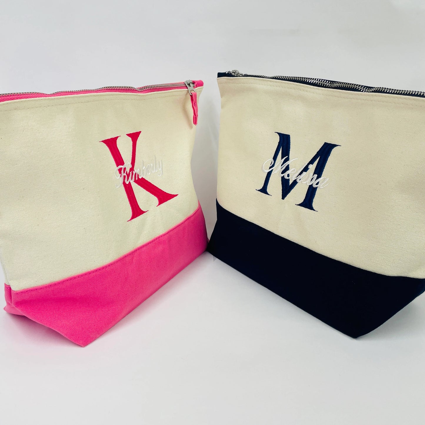 This picture shows two dipped accessory bags. Both bags have a silver zip.  One is mostly cream with a pink base and pink embroidered name. The other is mostly cream with a navy base and navy embroidered name. Available in two sizes, medium and large