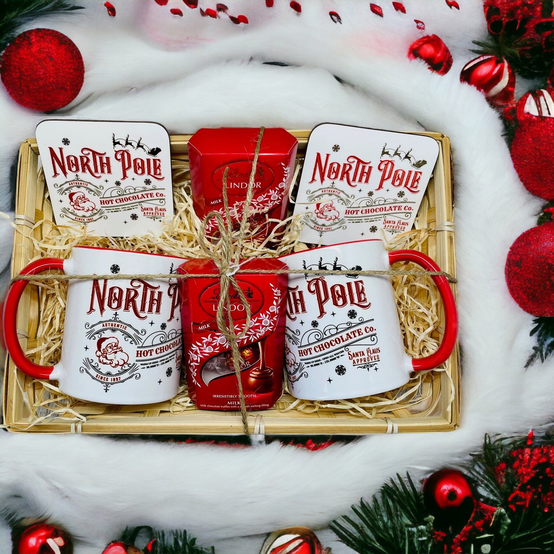 Christmas gift set in a wicker basket filled with a mug, coaster and Lindt chocolates. The design on the mug is a North Pole hot chocolate design. Giving the impression this is Santas hot chocolate. Ideal Christmas Eve gift. Stocking filler.