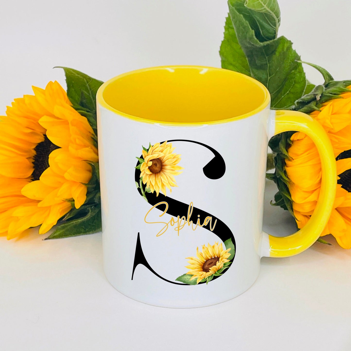 This is a bright, summery yellow inner and handle mug. This mug is printed with a black initial with a vibrant sunflower over it. The name is printed across the middle of the sunflower