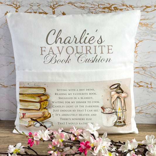 Luxury velvet book cushion. Printed on it is of a stack of books to the left and an oil lamp with a hot chocolate to the right. The bottom centre has a poem about reading.  The top half of the cushion has a name with favourite book cushion