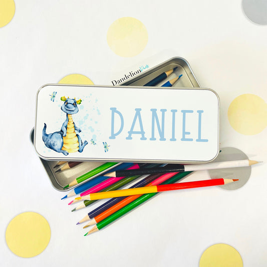 This is a metal rectangle pencil case for storing childrens pens and pencils. The tin is silver with a white lid. Printed on the lid is a blue dragon with dragonflies and also a name