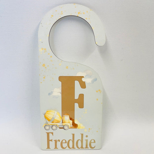 This is a lovely door sign with a very pale blue background. Featuring clouds and an initial. In front of the initial is a yellow construction vehicle and a name below.  Great personalised door hanger